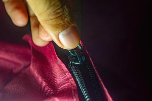 Close up on a hand zipping up a red fabric bag with a black zipper. The image captures the motion of securing the bag, emphasizing utility and convenience in a simple action photo