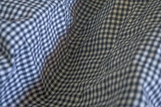 Close up on a blue and white gingham fabric with soft folds, creating a textured and patterned surface. The classic check pattern adds a timeless and versatile feel to the material photo