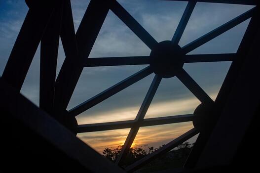 A low angle shot of a metal structure with geometric design against a sunset sky, creating a contrast between the industrial framework and the natural beauty of the horizon. photo