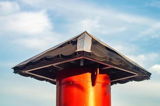 un rojo metal enviar con un cuadrado techo presentando oscuro herpes soportes en contra un azul cielo con suave nubes, creando un sencillo aún sorprendentes arquitectónico detalle al aire libre. foto