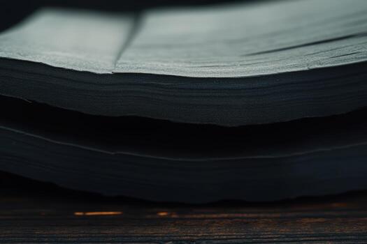 Stacked black pages resting on a wooden surface in a dimly lit space photo