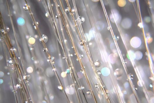 Close-up of delicate glass strands adorned with sparkling droplets reflecting soft multicolored lights creating an elegant and dreamy abstract background effect photo
