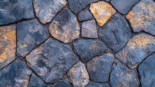 Close-up view of a textured stone wall. Dark gray and muted gold stones. Rough, irregular shapes. Natural pattern photo