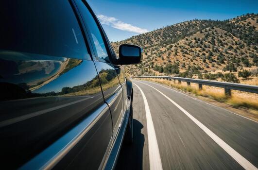 A black car is driving down a road with a beautiful view of the mountains in the background. The car is moving fast and the driver is focused on the road ahead photo