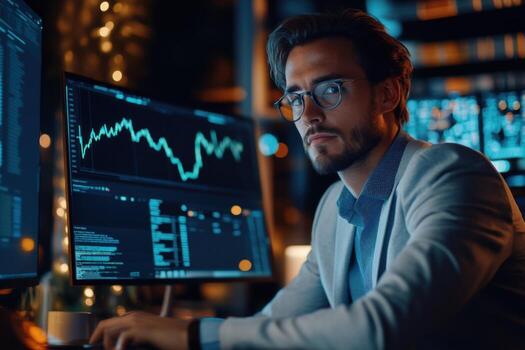 A man in a suit sitting at a desk with two computer screens photo