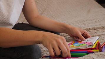 stänga upp se av en kvinna teckning vibrerande abstrakt former med vax kritor. de kreativ bearbeta utvecklas på en mjuk yta, visa upp lekfull färger och texturer medan hon fokuserar på henne konstverk video