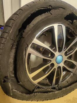 Damaged tire with broken wheel showing cracks, worn out automobile part in garage. photo