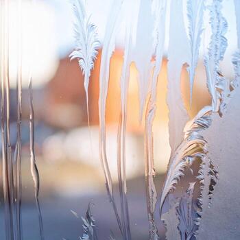 Frosted Window with Intricate Ice Patterns in Sunlight with Orange Building Visible through Glass photo