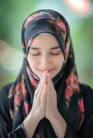 sereno mujer en hijab Orando con cerrado ojos foto