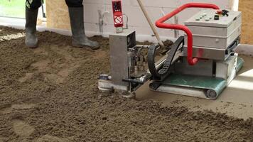 en arbetstagare fungerar en maskin med en röd hantera till nivå flytande skum betong screed. de interiör visar oavslutat väggar och stor fönster i rörelse. video