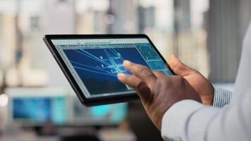 Close up of engineer using tablet to design power line towers in office. RD department specialist uses CAD software on device to optimize transmission tower systems, camera B video