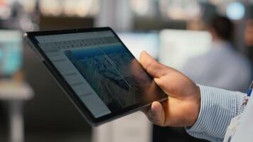 stänga upp av anställd håller på med digital modellering av vind energi generator redskap på enhet. tekniker i kontor använder sig av läsplatta till arbete på vind turbin cad design, håller på med grön energi forskning video