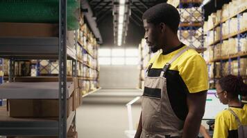 Warehouse worker inspecting cargo details on racks in a large scale fulfillment center, ensuring safety protocols in proper workwear. Logistics management and dispatch in action. Camera A. video