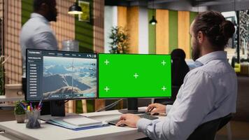 Worker uses green screen mockup PC to optimize advanced VAWT wind farm layout, enhancing clean energy production. Technician uses chroma key computer to do futuristic wind turbine simulation, camera A video