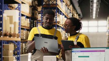 svart team medlemmar hantering paket data på bärbar dator för beställa bearbetning i logistik nav, verifierande pallar frakt etiketter för distribution protokoll. effektiv e-handel lager. kamera b. video