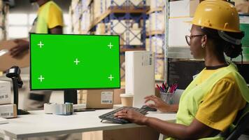 Frau im Sicherheit Weste Überprüfung Barcodes Etiketten Nächster zu Grün Bildschirm auf Computer, Arbeiten auf E-Commerce Verteilung Operationen und tragen Helm. groß Geschäft Lager Gestelle. Kamera b. video