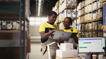 svart team medlemmar hantering paket data på bärbar dator för beställa bearbetning i logistik nav, verifierande pallar frakt etiketter för distribution protokoll. effektiv e-handel lager. kamera a. video