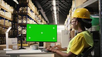 mujer en la seguridad chaleco comprobación códigos de barras etiquetas siguiente a verde pantalla en computadora, trabajando en comercio electrónico distribución operaciones y vistiendo casco. grande negocio almacenamiento bastidores cámara una. video