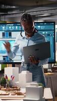 Vertical African american developer evaluating 3D models blueprints and digital software as part of strategic housing project in urban development area. City planning business project on tablet. Camera A. video