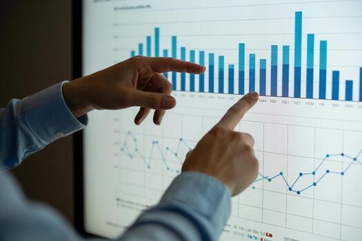 Two business analysts collaborate, reviewing financial data charts and graphs on a large screen display during a meeting, demonstrating teamwork and strategic planning for growth photo
