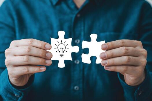 Person holding two puzzle pieces representing a bright idea, symbolizing innovation, connection, and problem-solving in a business or teamwork context photo