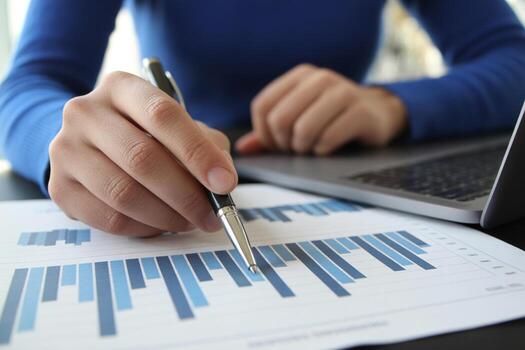 Close-up of a hand analyzing bar chart graphs with a pen, working on a laptop in a modern office, representing business analysis and financial growth photo