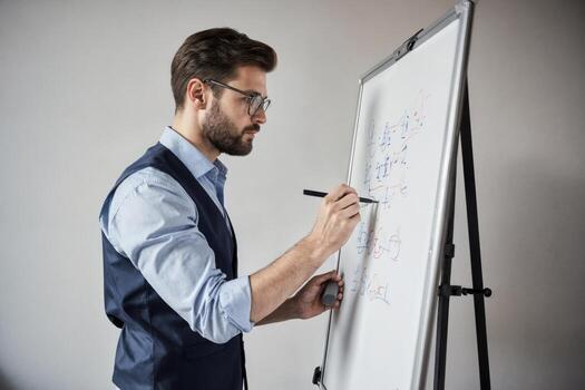 A man in a vest and tie is writing on a whiteboard photo