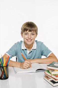 Child studying with books and colorful pencils at a table with a bright background during daytime photo
