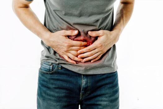 Man holding abdomen in discomfort due to stomach pain while standing against a plain background photo