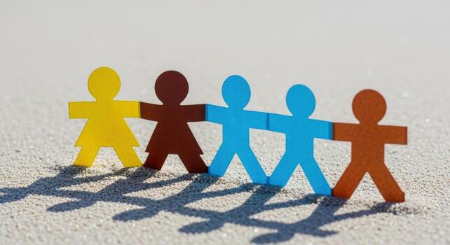 Colorful Paper Cutout Figures Holding Hands on Sand, Concept of Unity and Diversity photo