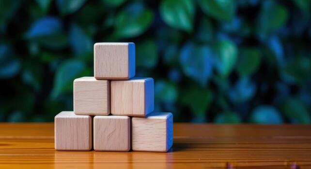 Wooden Blocks Stacked in Pyramid Shape on Wooden Surface Against Green Leaf Background photo