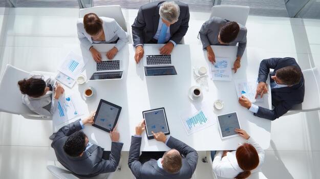 Diverse team having a meeting, using laptops and tablets, viewed from above, at bright modern office photo