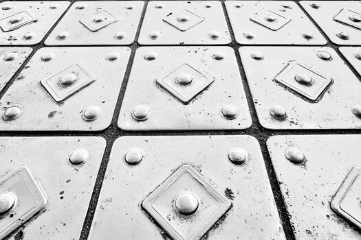 Metal plate flooring texture with raised patterns and rivets in black and white photo