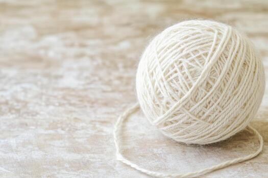 Soft white yarn ball resting on a textured surface in a crafting space photo