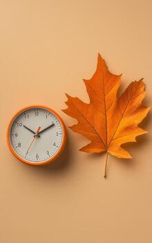 Orange Clock and Maple Leaf Create a Warm Autumn Ambiance on a Beige Background. photo