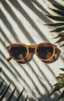 Stylish Wooden Sunglasses Placed on a Textured Surface With Shadow Patterns Created by Nearby Leaves photo