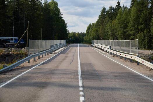 A long, empty highway lined with fencing and surrounded by trees in the background scenery photo