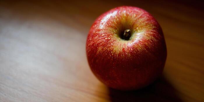 A glistening red apple rests on a wooden surface, captured in a close-up shot. photo