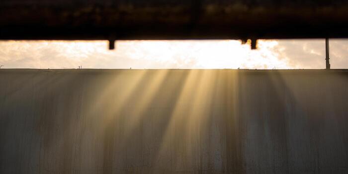 Golden sunlight streams dramatically over a wall, creating an alluring display of light and shadow. photo