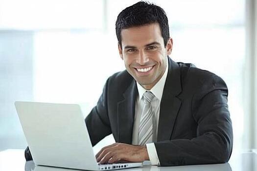 A smiling man in a suit sitting at a desk with a laptop photo