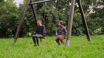 en un sereno patio de juegos, un joven madre interactúa alegremente con un niño en columpios, compartiendo la risa y sonrisas en medio de el verdor. sus un Perfecto excursión lleno con calor y conexión. video