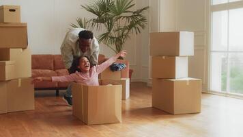 a africano americano família realocou para uma Novo apartamento, cercado de embalado caixas. uma pai tocam com uma criança, criando alegre recordações durante a comovente processo. video