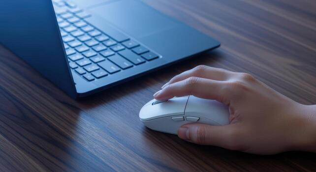 Womans Hand Using Wireless Mouse with Laptop on a Wooden Desk for Remote Work photo
