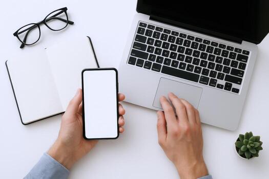 Overhead view of hands holding smartphone with laptop and notebook on white desk photo