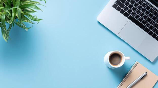 Modern workspace top view on blue background featuring laptop, notepad, coffee, and plant photo