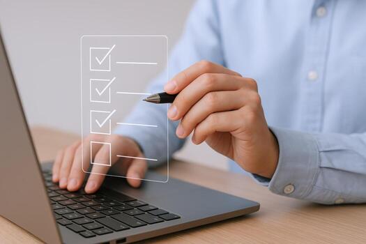 Completing Digital Checklist on Laptop Man with Pen Marking Tasks, Focus on Efficiency and Productivity photo