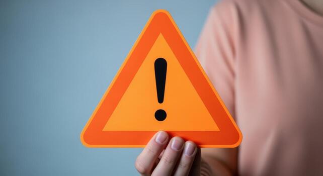 Person Holding an Orange Triangular Warning Sign with Exclamation Point, Hazard Awareness and Attention photo