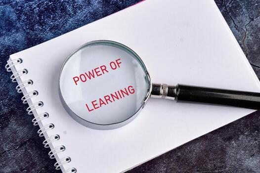 A magnifying glass focuses on the phrase power of learning written boldly on a notebook page, emphasizing its significance in education photo