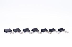 fila de negro aglutinante clips en blanco antecedentes oficina suministros estacionario. foto