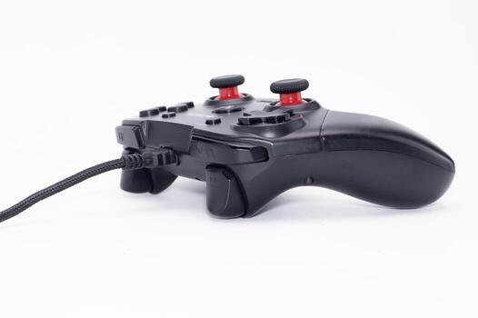 Black Wired Game Controller with Red Buttons on White Background Gaming Device. photo